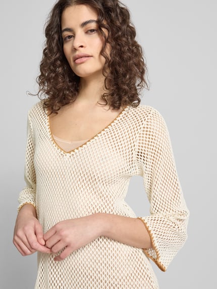 Modelka nosi Strickshirt mit V-Ausschnitt Modell 'OCTAVIE HAYATO' od Banana Moon z mieszanki bawełny, krój regular fit, dekolt w serek, rękaw o dł. 3/4, kremowa faktura siateczkowa z kontrastową lamówką, zbliżenie na górną część sylwetki, zdjęcie przód