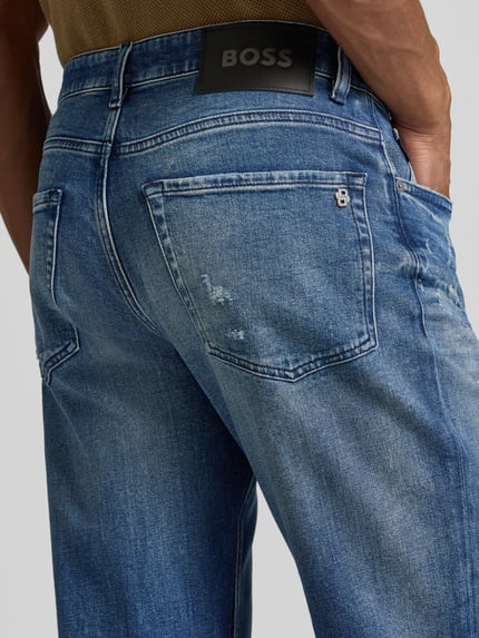 Männermodel draagt Regular Fit Straight Leg Jeans aus Baumwoll-Mix Modell 'RE.MAINE BO VISIBLE' van BOSS Orange, used-look, logodetail, labelstitching, 5-pocketmodel, denim, kleur: effen, detailaufnahme achterkant.