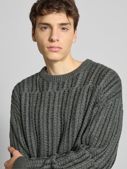 Männermodel trägt Relaxed Fit Strickpullover aus Baumwoll-Mix Modell 'FILL RLX' von Only & Sons, Zopfmuster, Nahaufnahme Oberkörper.