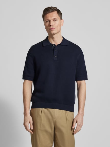 Männermodel trägt Relaxed Fit Poloshirt aus reine katoen Modell 'DANE' van SELECTED HOMME in uni gebreide look met label stitching, korte knoopsluiting, polokraag, V-hals, korte mouw met geribde zoom, strakke zoom onderaan, Ganzkörperansicht von vorne.