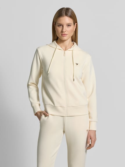 Frauenmodel trägt Sweatjacke mit Label-Applikation Modell 'OLYMPE' von Guess Activewear in Creme, glatte Struktur, Kapuze, Ganzkörperansicht von vorne.