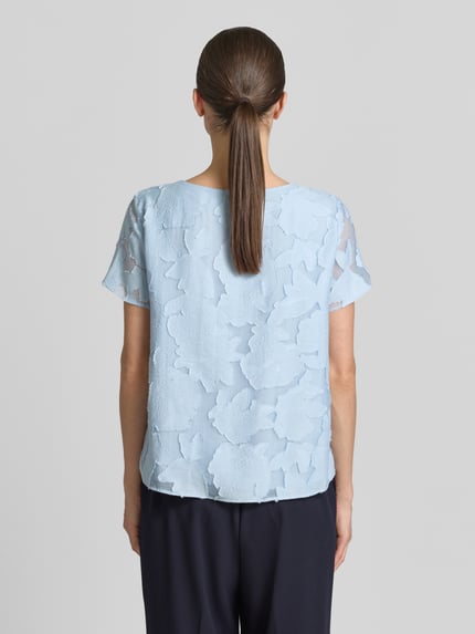 Frauenmodel trägt Blusenshirt aus Viskose-Mix mit Strukturmuster von More & More, hellblau, gerader Schnitt, Ganzkörperansicht Rückansicht.
