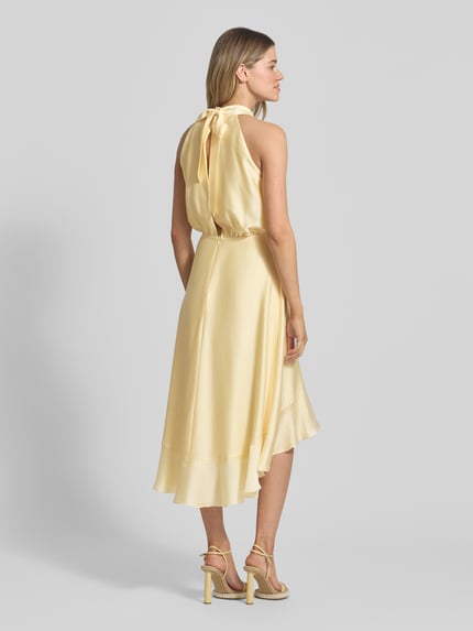 Frauenmodel trägt Neckholder-Cocktailkleid mit Volants von Swing aus Satin in sanftem Gelbton, Midikleid in A-Linie, Rückenansicht, Ganzkörperansicht Rückansicht, Rückenlänge bei Größe 36: 125 cm, Brustweite bei Größe 36: 34 cm.