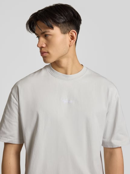 Männermodel trägt Oversized T-Shirt mit 1/2-Arm Modell 'Towson' von Pegador aus reiner Baumwolle, hellgrau, Nahaufnahme Oberkörper.