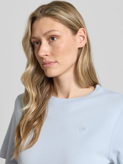Frauenmodel trägt Damen T-Shirt mit Logo-Stitching Modell 'SVEHA' von Oui aus reiner Baumwolle in Hellblau, Nahaufnahme Oberkörper.