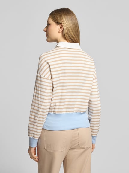 Frauenmodel trägt Regular Fit Poloshirt mit breitem Bund von Marc Cain in Beige-Weiß gestreift, hellblauer Bund, Ganzkörperansicht Rückansicht.