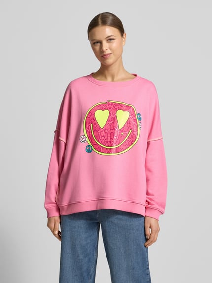 Frauenmodel trägt Oversized Sweatshirt mit Motiv-Print von miss goodlife in Rosa mit buntem Print, reine Baumwolle, Rundhalsausschnitt, Ganzkörperansicht von vorne.