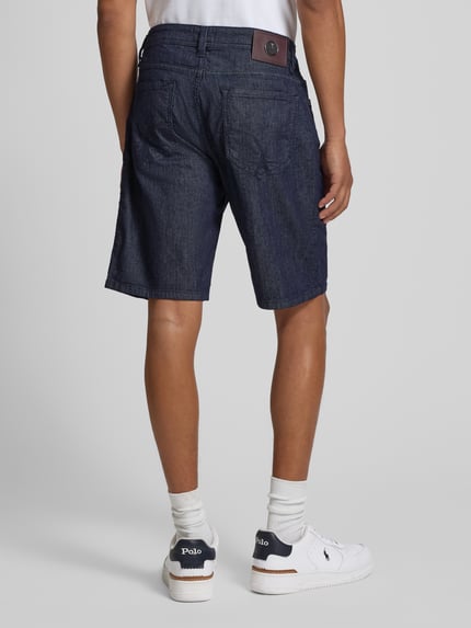 Męski model nosi Bermudas im 5-Pocket-Design Modell 'Fort' od JOOP! Collection, granatowy bawełniany materiał, krój straight fit, szorstka tekstura, szerokość w rozmiarze 32: 43 cm, długość wewnętrzna nogawki: 24 cm, pełny widok sylwetki z tyłu.