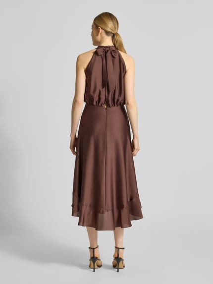 Modelka nosi Neckholder-Cocktailkleid mit Volants od Swing, satynowa tkanina, A-linia, midi, brąz, długość tyłu 125 cm, szerokość w rozmiarze 36: 34 cm, widok całej sylwetki od tyłu.