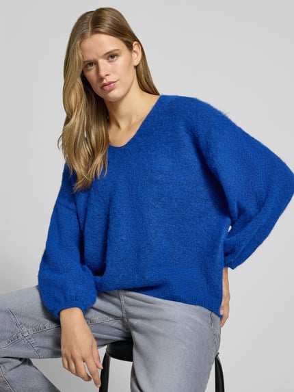 Frauenmodel trägt Pullover mit V-Ausschnitt Modell 'PCALLIE' von PIECES, meliertes Strickmaterial in Blau, elastische Bündchen, Nahaufnahme Oberkörper.