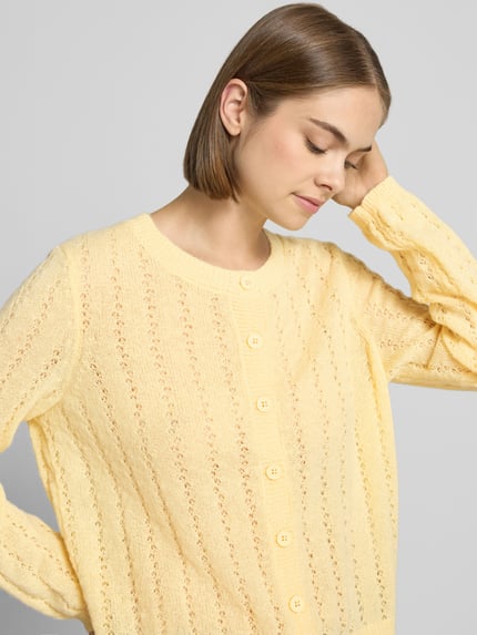 Frauenmodel trägt eine hellgelbe Regular Fit Strickjacke mit Rundhalsausschnitt Modell 'ADA' von PIECES, zarte Strickstruktur, Nahaufnahme Oberkörper. Damen Strickjacke von PIECES.