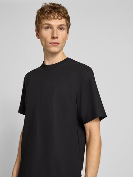 Męski model nosi t-shirt z elastycznej mieszanki materiałów z dodatkiem bawełny, prosty krój, model 'AUSTIN' od Jack & Jones, stójka, długość tyłu w rozmiarze M: 70 cm, kolor czarny, tekstura drobno prążkowana, zbliżenie na górną część ciała, widok z przodu.