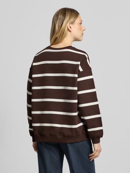 Modelka nosi 'Oversized Sweatshirt aus Baumwoll-Mix mit Statement-Stickerei' von Smith and Soul, brązowe i białe poziome pasy, krój oversized, mieszanka bawełny, prążkowane wykończenia, okrągły dekolt, widok całej sylwetki z tyłu.