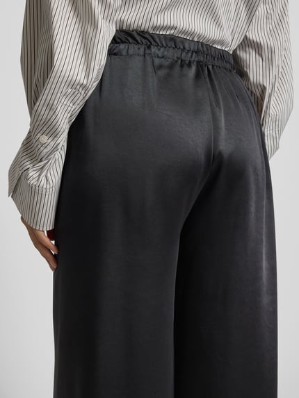 Frauenmodel trägt Wide Leg Stoffhose mit elastischem Bund von ZABAIONE, schwarze Farbe, glatte Textur, Detailaufnahme Rückenansicht.