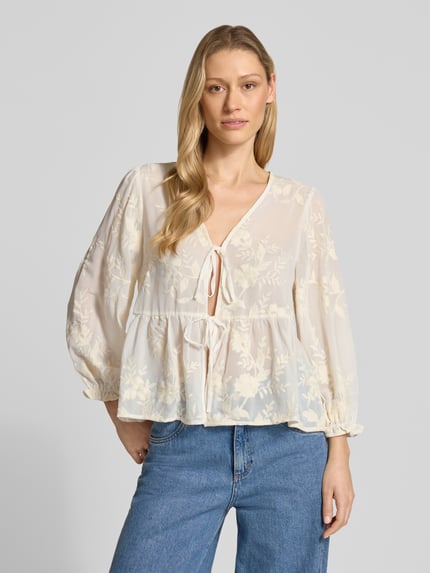 Modelka kobieca nosi Blusenshirt mit V-Ausschnitt von Apricot, prosty krój, dekolt w serek, wiązanie, bufiaste rękawy, długość tyłu w rozmiarze S: 55 cm, długość rękawów w rozmiarze S: 54 cm, jasne kolory, kwiatowy wzór, lekka tekstura, widok całej sylwetki z przodu.