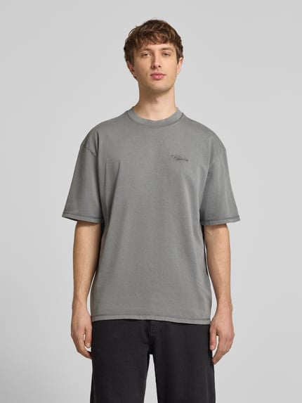 Männermodel trägt Oversized Fit T-Shirt mit Logo-Stitching von Pegador aus reiner Baumwolle in Grau, Rundhalsausschnitt, Ganzkörperansicht von vorne.