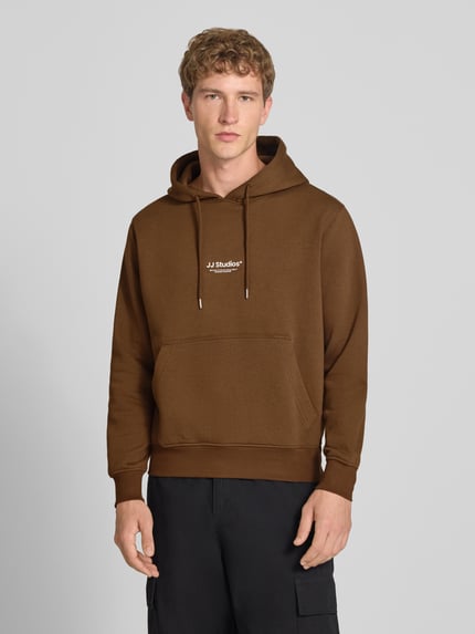 Männermodel trägt Regular Fit Hoodie aus Baumwoll-Mix Modell 'Soho' von JACK & JONES in Braun, Känguru-Tasche, Ganzkörperansicht von vorne.