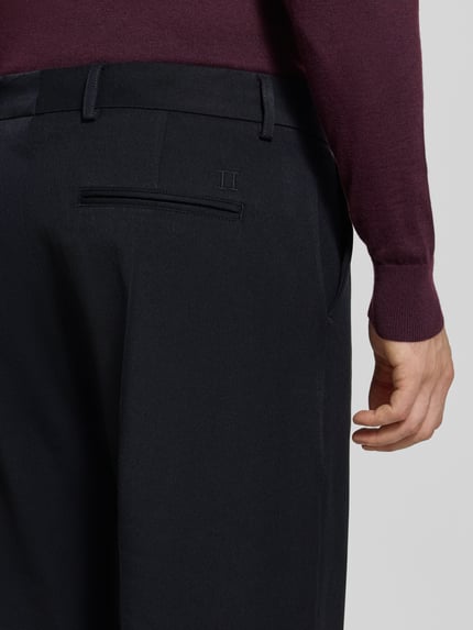 Männermodel trägt Stoffhose mit Bügelfalte und Eingrifftaschen von Les Deux in Dunkelblau, feine Textur, Detailaufnahme Rückansicht. Kontext: Herren Stoffhose von Les Deux, Material-Mix mit Viskose-Anteil, Straight Fit, Modell 'Roi', Knopf- und Reißverschluss, Französische Eingrifftaschen, Gesäßleistentaschen, Bundweite bei Größe 32: 46 cm, Innenbeinlänge bei Größe 32: 77 cm.