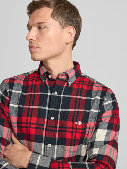 Männermodel trägt Freizeithemd mit Knopfleiste von Gant, kariert in Rot, Schwarz, Weiß, Regular Fit, Baumwolle, Brusttasche, Nahaufnahme Oberkörper.
