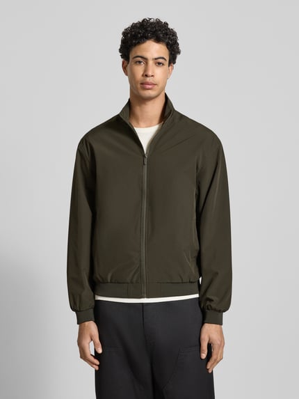 Męski model nosi Regular Fit Jacke mit Stehkragen Modell 'Charge' od Jack & Jones, zamek, kieszenie, elastyczne wykończenia, kolor oliwkowy, krój regular fit, Szerokość w rozmiarze M: 50 cm, długość tyłu: 66 cm, długość rękawa: 64 cm, szerokość ramion: 49 cm, całopostaciowy widok z przodu.