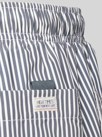 Produktfoto, Badehose mit Gesäßtasche und Label-Patch von MCNEAL mit dunkelblauen und weißen Streifen, elastischer Bund, Detailaufnahme.