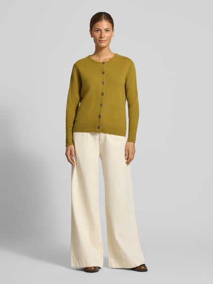 Frauenmodel trägt Cardigan aus Wolle mit Rundhalsausschnitt von Christian Berg Woman in Olivgrün, Regular Fit, Knopfleiste, cremefarbene weite Hose, lockere Struktur, Ganzkörperansicht von vorne.