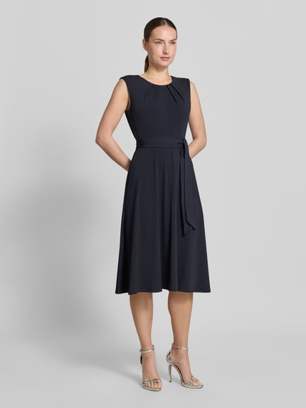 Frauenmodel trägt Cocktailkleid mit Bindegürtel von Christian Berg Woman Selection in Dunkelblau, taillierte Passform, Ganzkörperansicht von vorne.