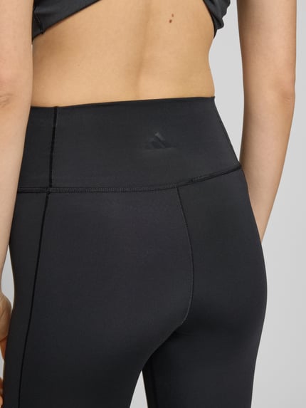 Frauenmodel trägt Flared Fit Stoffhose mit breitem Bund Modell 'All Me' von adidas Sportswear in Schwarz, elastischer Material-Mix, Nahaufnahme Rückenansicht.