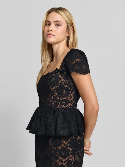 Frauenmodel trägt ein schwarzes, florales Abendkleid mit Spitzenpeplum von Self-Portrait, Spitzenstruktur, Etui-Passform, Nahaufnahme Oberkörper.