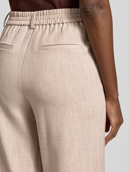 Frauenmodel trägt High Waist Hose Modell 'VARONE' von Vila in Beige mit feiner Struktur, Material-Mix mit Viskose-Anteil, Detailaufnahme Rückansicht.