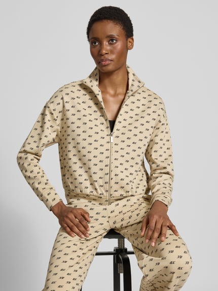 Frauenmodel trägt Sweatjacke mit Reißverschluss von Armani Exchange aus Baumwoll-Mix, beiger Stoff mit Allover-Label-Print, Nahaufnahme Oberkörper.