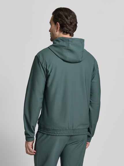 Męski model nosi Regular Fit Sweatjacke mit Logo-Patch od EA7 Emporio Armani, elastyczna mieszanka materiałów, fakturowany wzór, kaptur z tunelem, wpuszczane kieszenie, zamek błyskawiczny dwustronny, elastyczne wykończenia, długość tyłu 68 cm, długość rękawów 67 cm, widok całej sylwetki z tyłu.