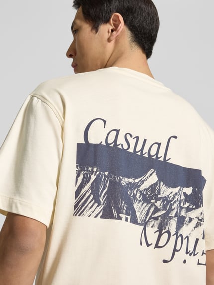 Männermodel trägt Herren T-Shirt aus reiner Baumwolle Modell 'KARLBERG' von Casual Friday in Beige mit Label-Print, Nahaufnahme Rückansicht. Rückenlänge bei Größe M: 67 cm, lockere Passform, Rundhalsausschnitt, Label-Stitching.