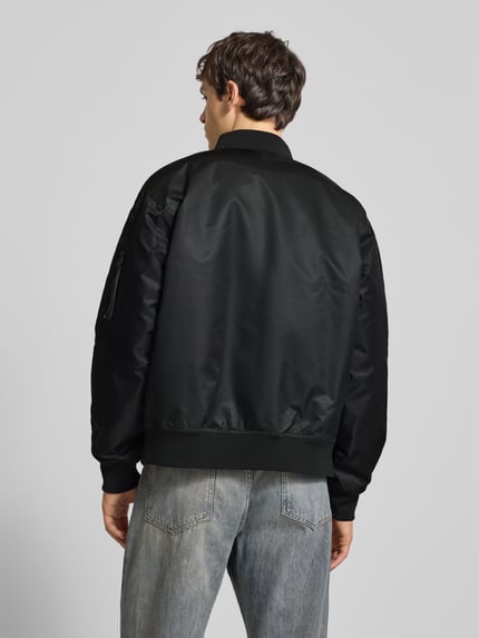 Männermodel trägt Bomberjacke mit Label-Stitching von Calvin Klein Jeans in Schwarz, glatte Struktur, Regular Fit, Ganzkörperansicht Rückansicht.