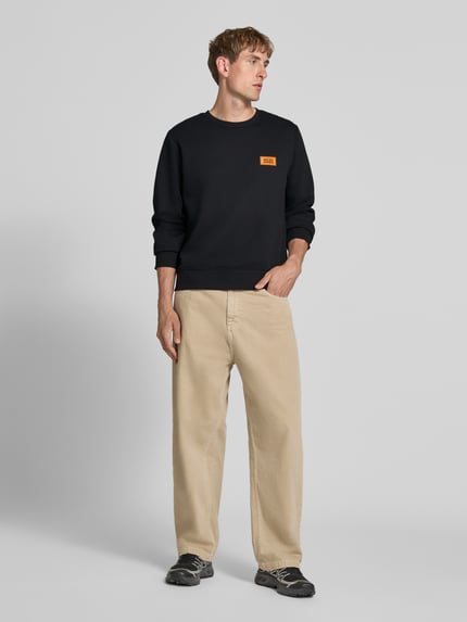 Męski model nosi bluzę z mieszanki bawełny o luźnym kroju, okrągłym dekolcie i nadruku z logo, Model 'RUSH' od JACK & JONES, długość tyłu 67 cm, długość rękawów 67 cm, prążkowane wykończenia, widok całej sylwetki z przodu.
