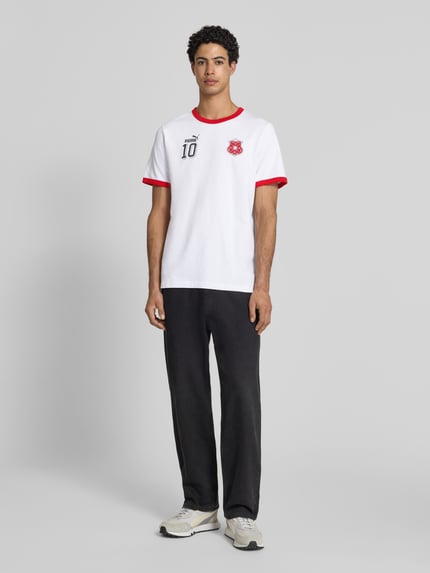 Männermodel trägt weißes Herren T-Shirt aus Baumwolle Modell 'FUTURE' von PUMA PERFORMANCE mit roten Details, gerader Schnitt, Rundhalsausschnitt, Label-Details, Ganzkörperansicht von vorne.