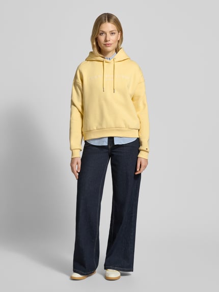 Vrouwenmodel draagt Relaxed Fit Hoodie uit katoenmix van Tommy Hilfiger, effen geel, label stitching, capuchon, lange mouwen, sweatstof. Volledige lichaamsvooraanzicht.