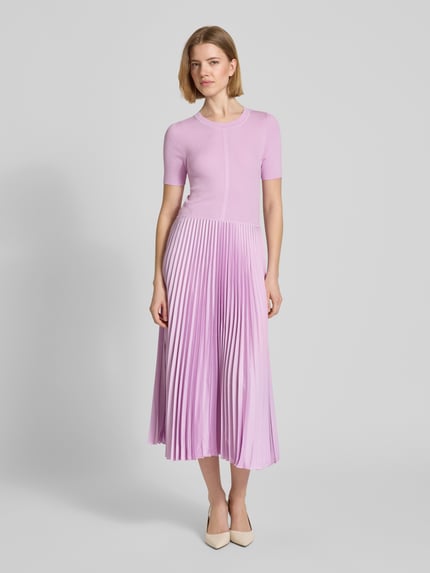 Vrouwenmodel draagt tailliertes Businesskleid aus Viskose-Mix Modell 'FADRIDI' van BOSS, effen look, taillering fit, midi-lengte, ronde hals, plissé-details, korte mouw, rechte zoom, pastel lila tinten, gladde en geplisseerde texturen. Volledige lichaamsaanzicht van voren.