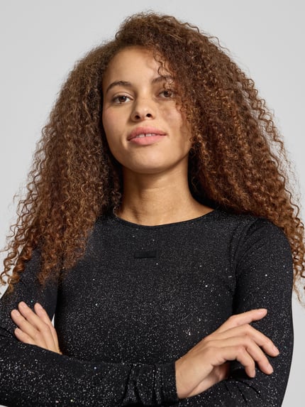 Frauenmodel trägt Cropped Longsleeve mit Label-Detail von Karo Kauer in Schwarz mit Glitzer, Rundhalsausschnitt, Material-Mix, Nahaufnahme Oberkörper.