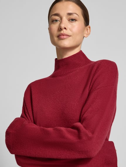 Frauenmodel trägt Strickpullover mit Stehkragen von Christian Berg Woman in Rot, reine Baumwolle, weite Ärmel, Nahaufnahme Oberkörper.