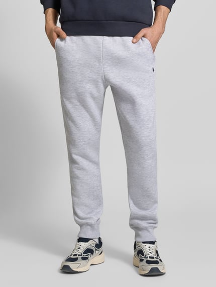 Männermodel trägt Slim Fit Sweatpants mit Logo-Stitching von REVIEW aus Baumwoll-Mix in Hellgrau, elastischer Bund, Gesäßtasche, Ganzkörperansicht von vorne.