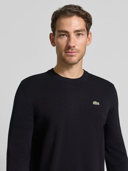 Männermodel trägt schwarzen Regular Fit Pullover aus Baumwoll-Mix von Lacoste, dezentes Lacoste-Logo, Nahaufnahme Oberkörper.