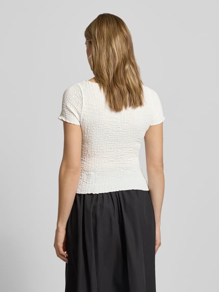 Frauenmodel trägt Slim Fit T-Shirt mit Strukturmuster Modell 'Alora' von Noisy May, cremeweiß, Elastischer-Material-Mix, Kurzärmelig, U-Boot-Ausschnitt, Rückenlänge bei Größe S: 50 cm, Ganzkörperansicht Rückansicht.