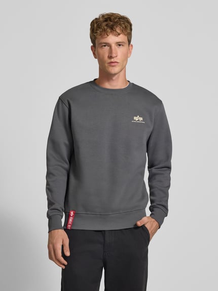 Männermodel trägt Sweatshirt mit Label-Details von Alpha Industries in Grau mit gerippten Abschlüssen, Ganzkörperansicht von vorne. Baumwoll-Mix, gerader Schnitt, Rundhalsausschnitt, Rückenlänge 69 cm, Ärmellänge 72 cm.