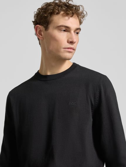 Mannermodel draagt Regular Fit Strickpullover aus reiner Baumwolle Modell 'UPCAS' van BOSS, zwart, fijne breistructuur, label stitching, crew neck, lange mouw, geribde boorden, nahaufnahme bovenlichaam.