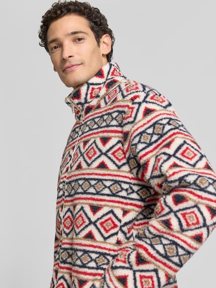 Männermodel trägt Regular Fit Fleecejacke mit Stehkragen von MCNEAL, grafisches Muster in Rot, Blau und Beige, Teddyfell, Nahaufnahme Oberkörper.