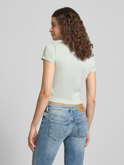 Kobiece modelka nosi Slim Fit cropped T-Shirt aus Baumwoll-Mix Modell 'BABY TEE_B' od HUGO, damski t-shirt, jasne kolory, tekstura gładka, prosty fason, widok całej sylwetki z tyłu, kontekst: damski t-shirt od HUGO Blue.
