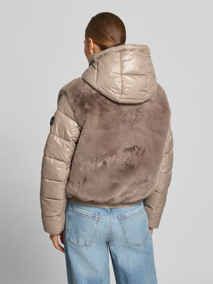 Frauenmodel trägt Steppjacke mit Kunstfell-Besatz Modell 'ONIKA' von khujo in Taupe, glänzende und weiche Texturen, Ganzkörperansicht Rückansicht. Regular Fit, Kapuze mit Tunnelzug, Zweiwege-Reißverschluss, Rückenlänge 55 cm, Schulterbreite 44 cm, Brustweite 47 cm, Ärmellänge 65 cm.