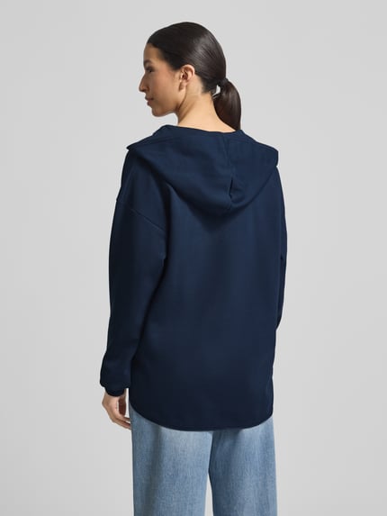 Frauenmodel trägt Oversized Hoodie aus Baumwoll-Mix Modell 'Tristani' von JOOP! in Dunkelblau mit Kapuze, verlängerte Rückseite, Ganzkörperansicht Rückansicht.