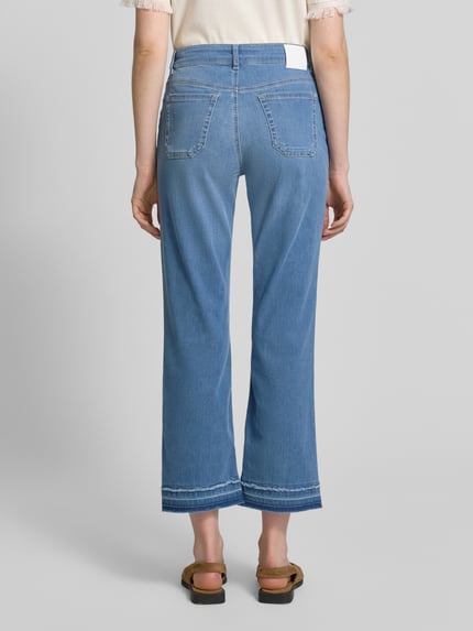Kobiece modelka nosi Straight Leg Jeans mit Fransensaum od Marc Cain, mieszanka bawełny i lyocellu, krój straight fit, wpuszczane kieszenie, frędzle na dole, kieszenie z tyłu, szerokość w rozmiarze 36: 37 cm, długość wewnętrzna nogawki w rozmiarze 36: 70 cm, widok całej sylwetki z tyłu.